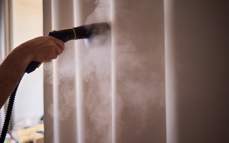 Professional technician steam cleaning white curtains to prevent damage.