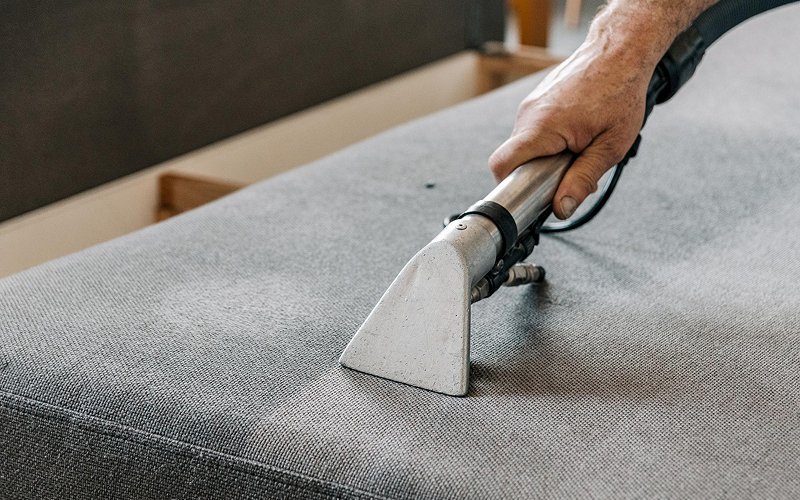 Professional deep cleaning a fabric sofa to remove stains.