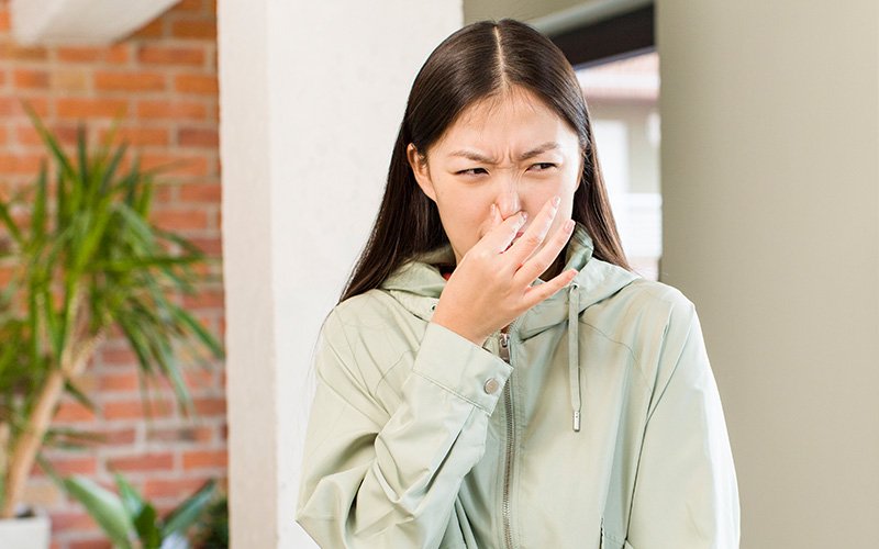 Person holding nose reacting to bad smell.