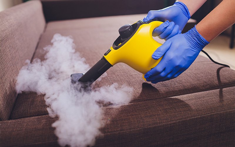 Professional steam cleaning a fabric sofa.