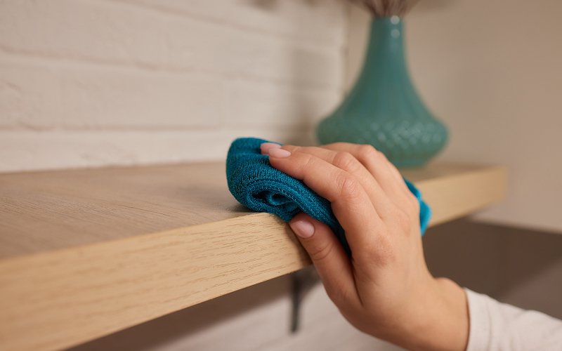 Hand wiping wooden furniture to clean and remove surface pollutants.