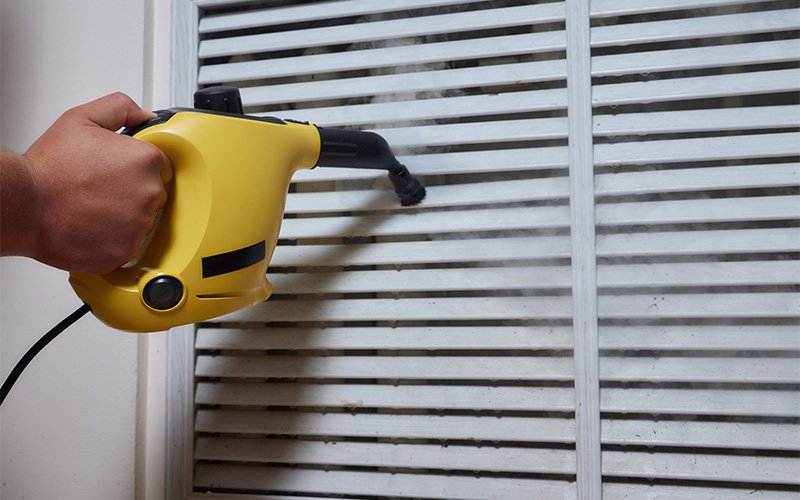 Person cleaning window blinds with steam cleaner.