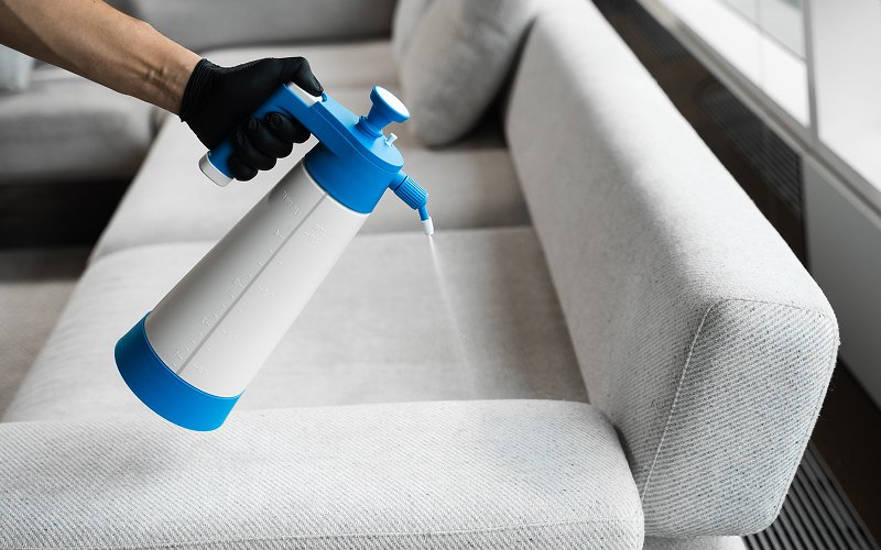 Gloved hand spraying treatment to remove formaldehyde from fabric sofa.