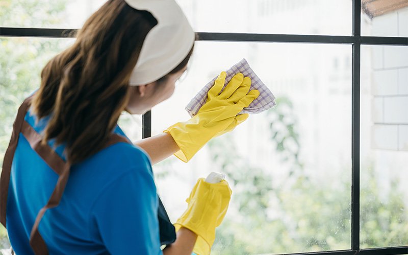 Domestic worker wiping down residential window frames safely.