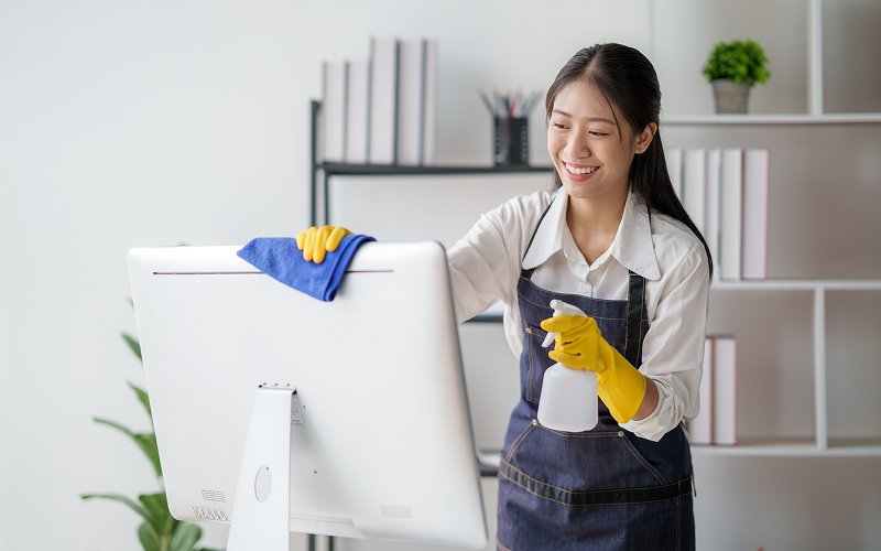 Janitor wiping computer monitor to provide office cleaning services.