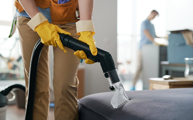Professional cleaner vacuuming post renovation dust from a fabric sofa.