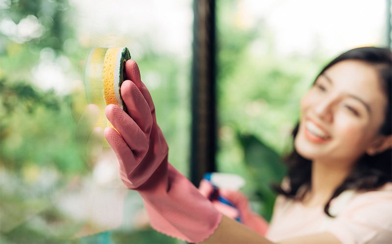 Woman wearing pink gloves cleaning an interior window pane.